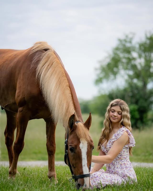 Rylee Eilerman kneels beside Sonny, a flaxen-maned chestnut, as he grazes in a green field.